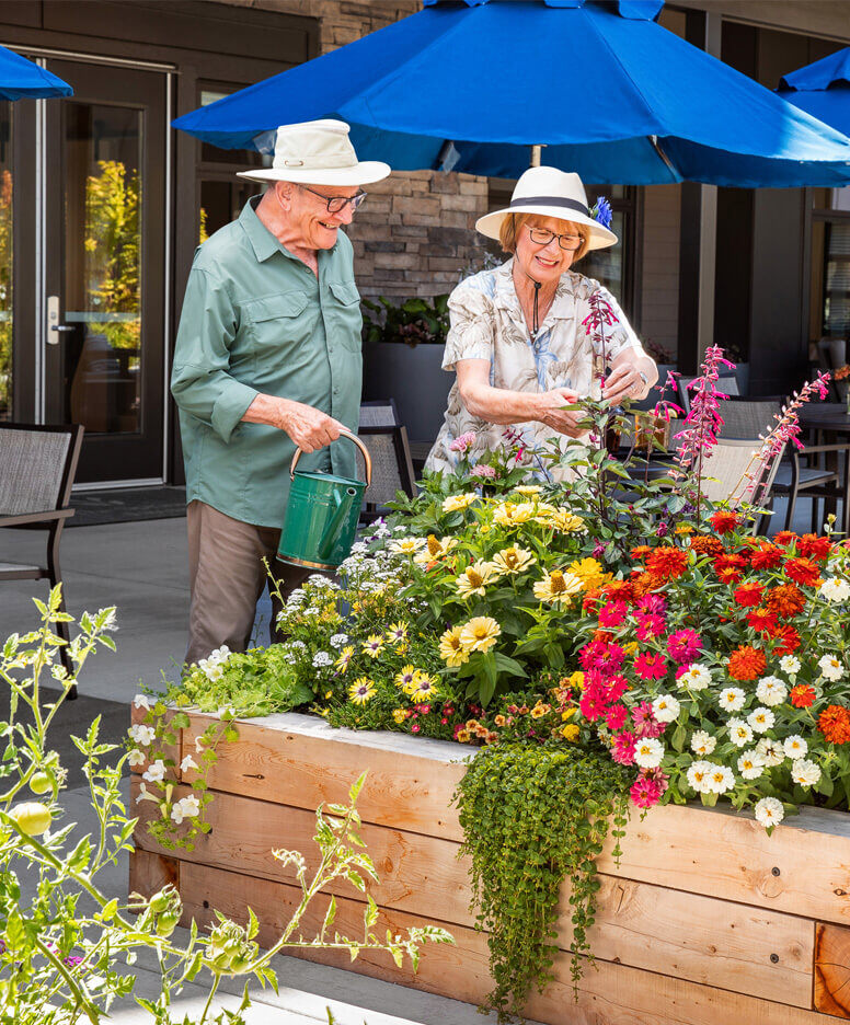 Two senior living residents gardening and smiling together.