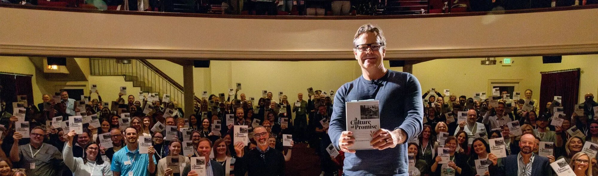 Man holding up a book in front of a crowd
