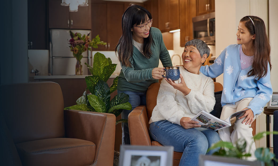 Woman handing her mother a cup of coffee while she is seated next to her grandaughter