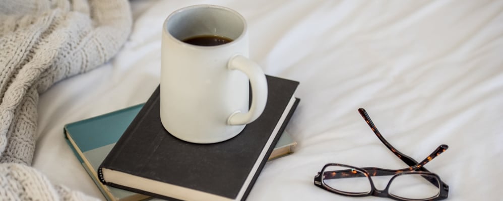 Books, coffee mug, and glasses resting on a bed at The Springs at Lancaster Village in Salem, Oregon