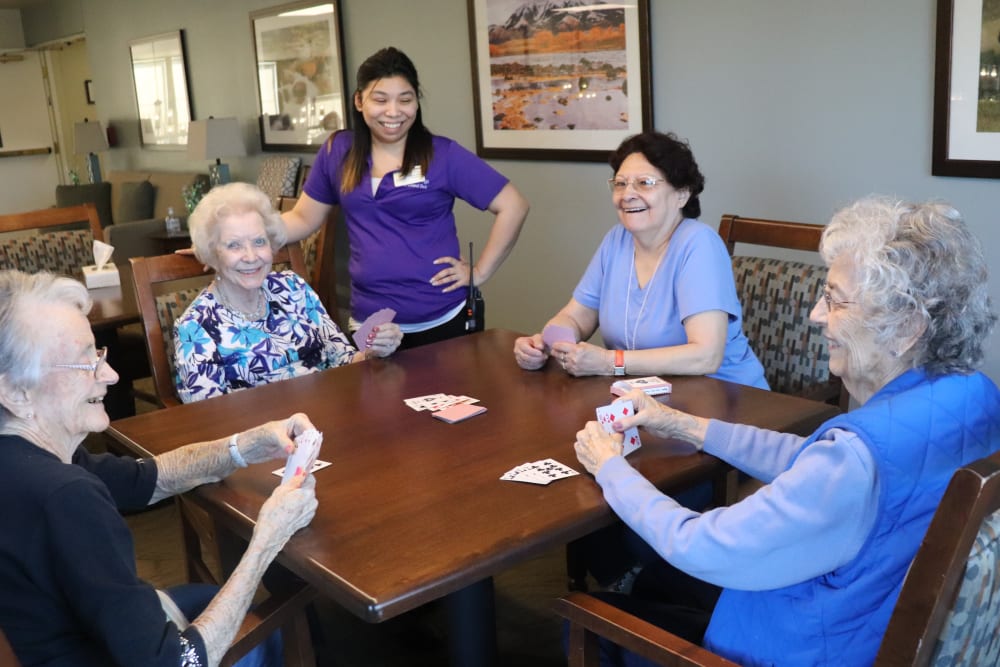 Four friends playing cards with a caregiver looking on and smiling at The Springs at Grand Park in Billings, Montana