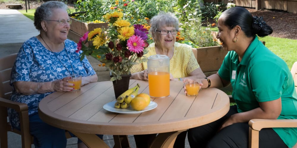 Two residents enjoying a beverage with an employee outside at wood table complete with sunflower centerpiece at The Springs at Willowcreek in Salem, Oregon