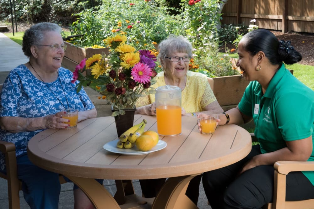 Two residents sitting outside enjoying a beverage with a staff member on a sunny day complete with sunflower centerpiece at The Springs at Willowcreek in Salem, Oregon