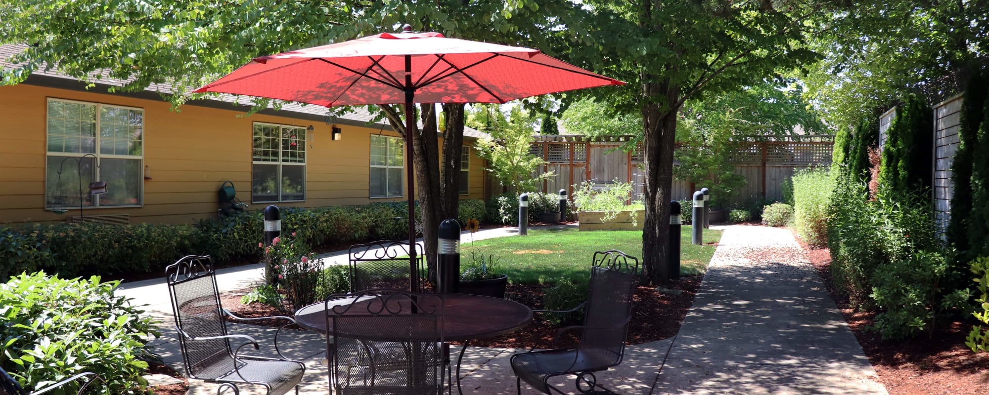 Porch area outside of upscale senior living apartment complete with patio seating and red umbrella at The Springs at Willowcreek senior living in Salem, Oregon